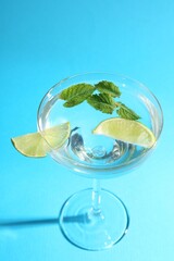 Martini cocktail with slices of lime and mint on light blue background, closeup