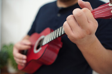 Asian man playing ukulele at home