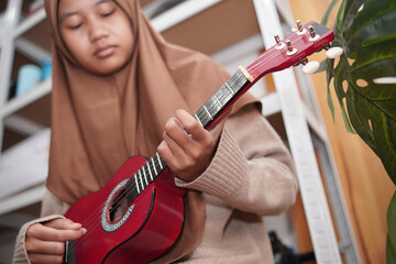 Asian muslim woman playing ukulele