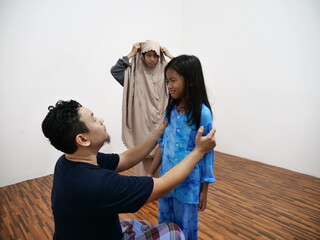Asian muslim father put on clothes to his daughter to do salah prayer, preparation for islamic pray