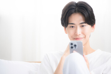 Close-up of a young man smiling as he operates his smartphone
