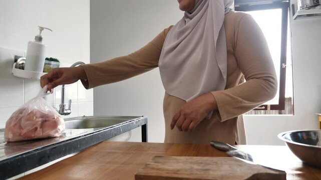 Asian muslim woman taking chicken meat out of plastic groceries bag