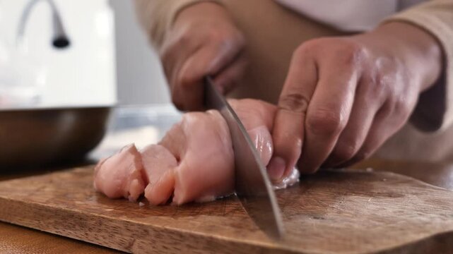Asian muslim woman cutting chicken breast meat. Meal preparation