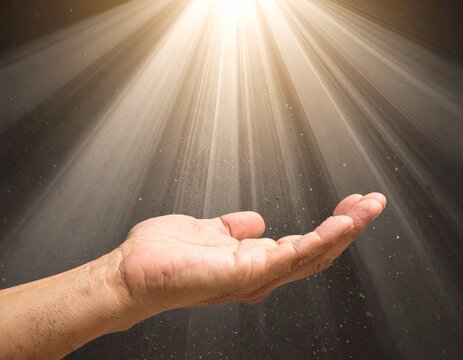 Mano extendida hacia un haz de luz brillante que entra desde arriba