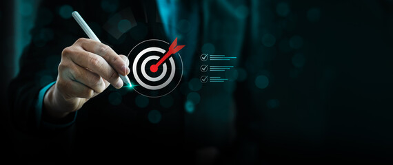 Business goal setting concept with businessman using digital stylus to target center of dartboard,...