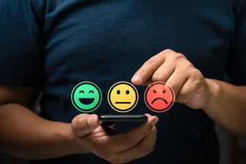 Customer satisfaction feedback concept showing person using mobile phone to select emotion face...