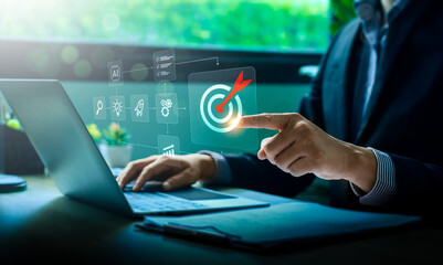 Businessman using laptop with virtual interface showing target icon and strategic planning process, symbolizing digital goal setting, project management, artificial intelligence, and business success