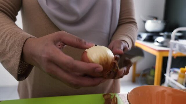 Asian muslim woman peeling, cutting and slicing onion and garlic. Preparing marinade for chicken meat