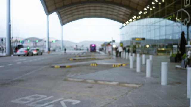 Blurred view of individuals at outdoor airport terminal with buses and cars visible under a canopy.