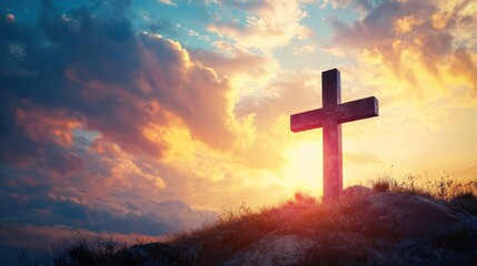 A wooden cross stands on a hilltop at sunset, with a dramatic sky filled with clouds and a warm, golden light illuminating the scene.