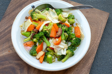 Stir-fried mixed vegetables served on a white plate with a spoon, showcasing vibrant colors and fresh texture in a clean, rustic setting.