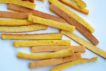 A pile of long, yellow, crunchy toast sticks is scattered on a clean white background.