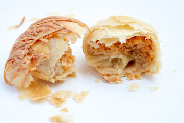 A golden-flaky pia pastry, torn in half to reveal the savory filling and texture inside. The close-up shot on a white background captures the rustic details of this traditional Indonesian snack.