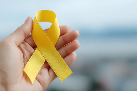 Hand holding a vibrant yellow ribbon symbolizes the ongoing fight against childhood cancer and sarcoma, spreading awareness and hope