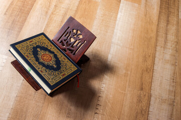 Top Down View Of Closed Qur'an Resting On Traditional Wooden Stand On Hardwood Floor