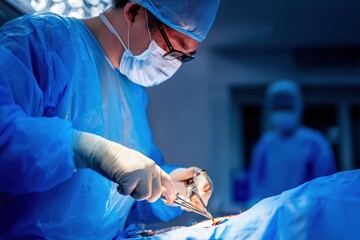 Professional surgeon wearing surgical mask, cap and gloves performing surgery using surgical instruments in operating room