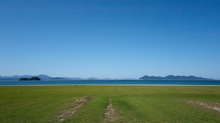 Fototapeta premium Large green meadow with small islands in foreground and clear blue sea view under cloudless sky. Green space management landscape for lawn care product advertisement.