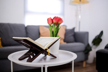 A Holy Quran Open On A Wooden Stand, Next To A Vase Of Red Tulips In A Modern Home