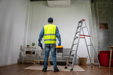 Air conditioner repair: A technician inspects an air conditioner, ladder and interior setting, this image speaks to the importance of maintenance and the skill required to service them.
