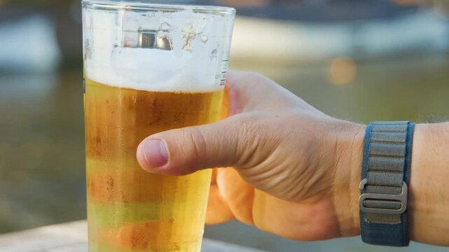 Hand Lifting Pint Glass of Beer by Riverside