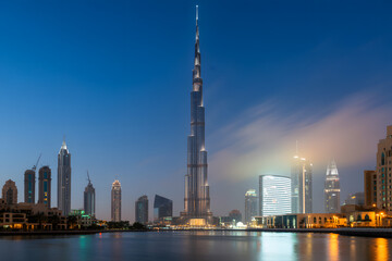 Obraz premium Majestic Skyscraper's Skyline View: An expansive, bird's-eye view of a tall, imposing skyscraper rises dramatically, dominating a cityscape, captured during the twilight hours and under a clear, blue.