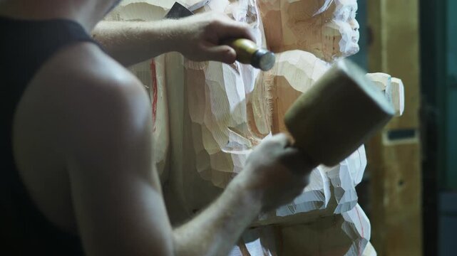 Wood sculptor strikes with a mallet and guides a chisel to refine a statue, showing the strength, precision, and artistry of traditional wood carving in progress.