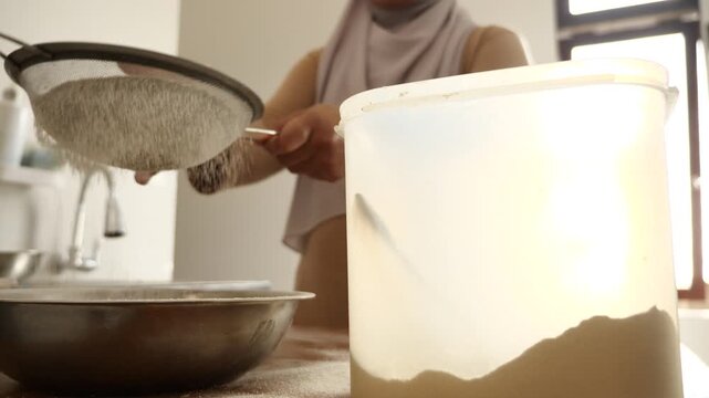 Asian muslim woman sifting flour to make spiced breaded chicken or bread baking