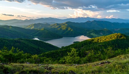 Naklejka premium Panoramic view of a serene lake nestled within a valley of verdant mountains at sunset.