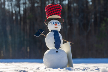 Business Snowman talking on smartphone in snowy landscape. Snowman making a business phone call. Funny snowman hacker using laptop outdoors. Snowman with mobile phone during winter celebration.