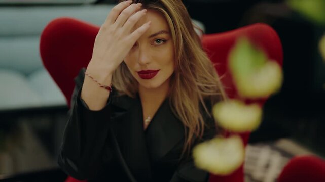 Elegant woman wearing black outfit and red lipstick, sitting in red chair with a confident expression in an urban setting. Ideal for lifestyle or fashion-related images. Beautiful Young Woman
