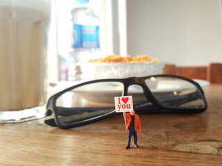 Miniature toy of mini action figure of people hanging the poster with text "I LOVE YOU". Blurred view on the brown table at coffee shop and blurred background. Romantic photography concept design.