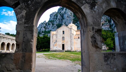 Fototapeta premium An ancient stone church, framed by arched openings, stands amidst a grassy courtyard, bathed in natural light.