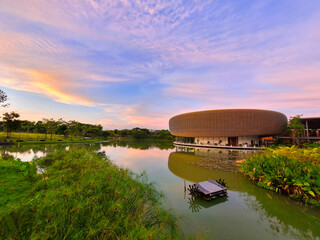 A modern, luxurious circular architecture building with a sunset sky over the river