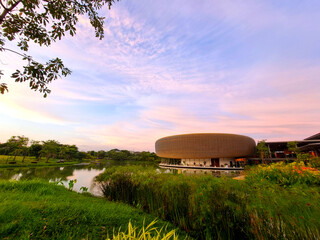 A modern, luxurious circular architecture building with a sunset sky over the river