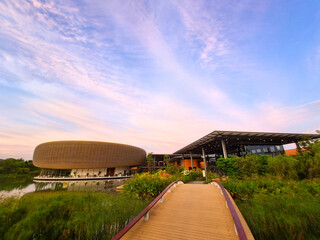 A bridge crosses the river to a circular building, a luxurious modern architecture, and a sunset sky along the river