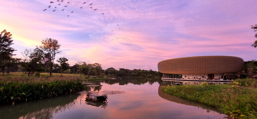A modern, luxurious circular architecture building with a sunset sky over the river