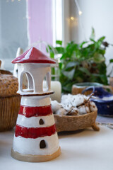 handcrafted ceramic lighthouse stands on table, surrounded by plants and various decorative items. lighthouse features bold red white stripes, adding charm space. vertical. selective focus. close up.