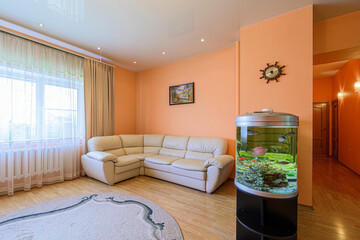 cozy room features a beige sectional sofa, round rug, and an eye-catching aquarium. Walls are peach, and a window offers natural light