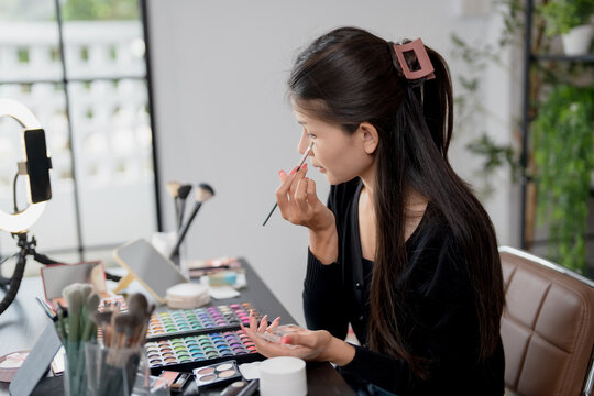 Asia woman beauty influencer makeup artist vlogger live streaming makeup tutorial on smartphone for social media