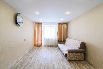 Cozy room with a sofa, curtains, and wall clock. Neutral colors, wooden floor