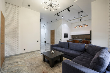 modern living room featuring a blue sectional sofa, a dark coffee table with a white sculpture, marble-like flooring, and a view into the kitchen area with overhead lighting