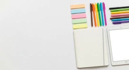 Top-down view of a blank notebook, tablet, colorful markers, and sticky notes arranged on a white surface.