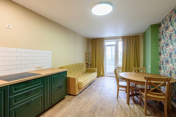 Cozy apartment interior.  Green kitchen cabinets, yellow sofa, and round wood table set against a muted color scheme with floral wallpaper accent