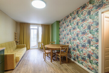 bright living room with a round wooden table, green sofa, and floral wallpaper. The room has a light, airy feel