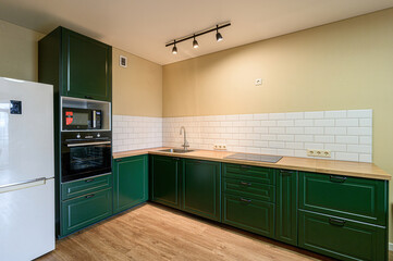 Fototapeta premium Modern kitchen with dark green cabinets, light wood countertops, white tiled backsplash, and stainless steel appliances