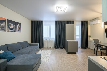modern living room with a gray sofa, dark curtains, artwork on the wall, and a compact kitchen area