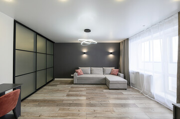 modern living room with a grey sofa, wood floors, and a dark accent wall. Features a large window and stylish lighting