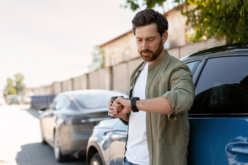 Businessman checking time and drinking coffee near his car in the city
