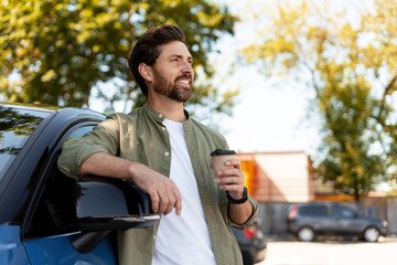 Happy man drinking coffee outside his car in a parking lot