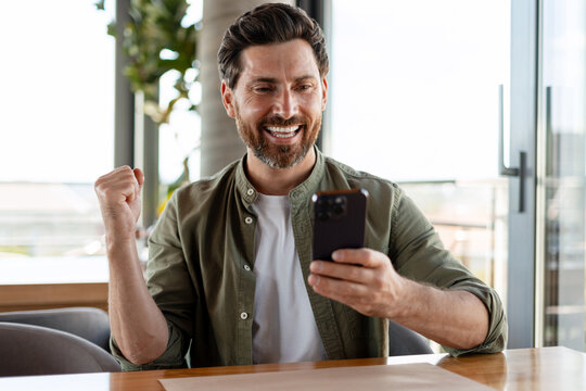 Excited businessman celebrating success while using mobile phone in restaurant